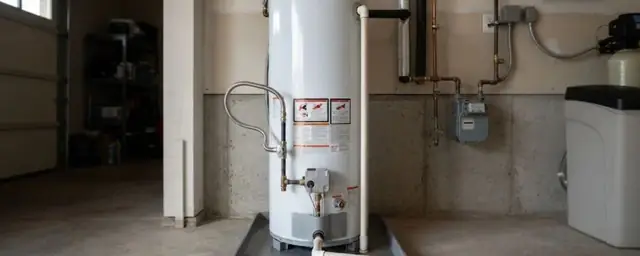 Gas tank water heater in a garage sitting in a drain pan with a gas meter nearby